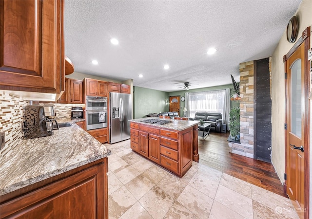 kitchen featuring ceiling fan, a center island, light stone counters, a textured ceiling, and appliances with stainless steel finishes