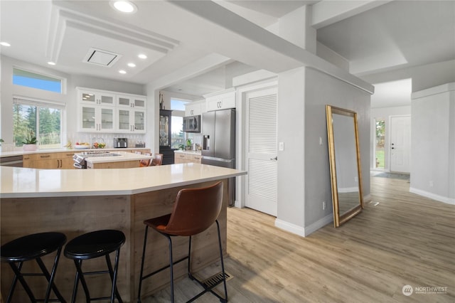 kitchen featuring white cabinets, a kitchen bar, light wood-type flooring, and appliances with stainless steel finishes