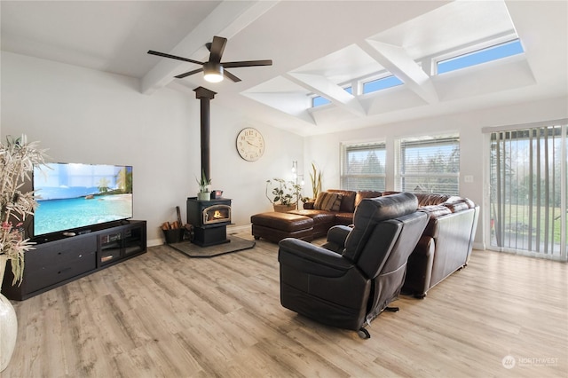 living room featuring a wood stove, ceiling fan, beamed ceiling, and light wood-type flooring