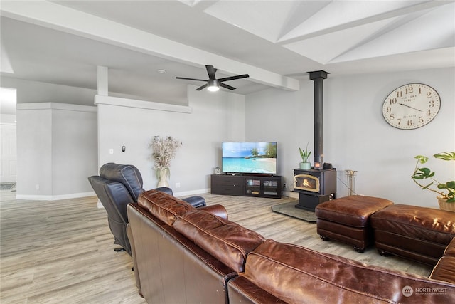 living room with a wood stove, ceiling fan, vaulted ceiling with beams, and light wood-type flooring