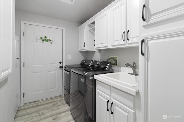 laundry area with light hardwood / wood-style floors, cabinets, separate washer and dryer, and sink