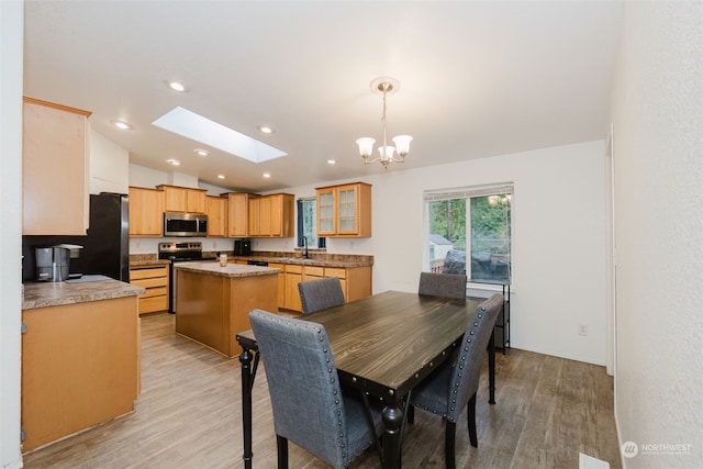 dining area with vaulted ceiling with skylight, a notable chandelier, sink, and light hardwood / wood-style flooring