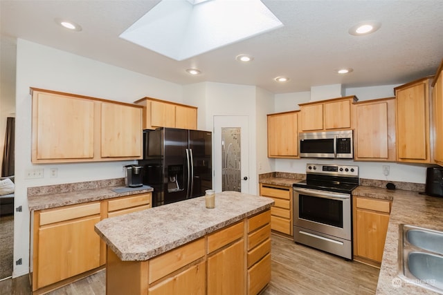 kitchen with appliances with stainless steel finishes, a center island, a skylight, and light hardwood / wood-style flooring