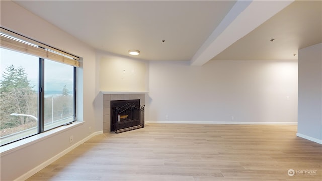 unfurnished living room with beam ceiling, light wood-type flooring, and a tile fireplace