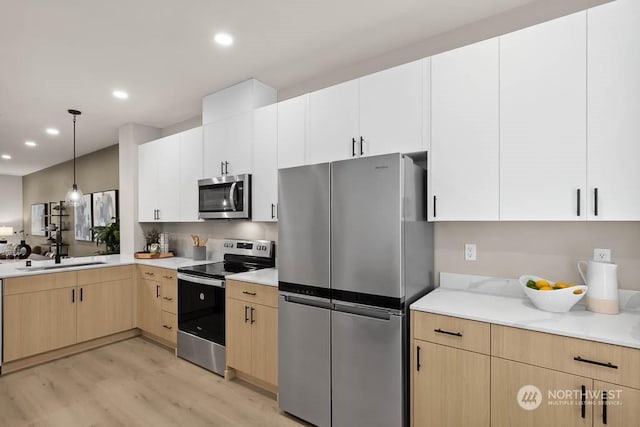 kitchen with stainless steel appliances, white cabinetry, light hardwood / wood-style floors, and sink