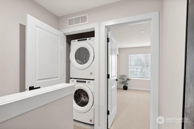 laundry area featuring light colored carpet and stacked washer / dryer