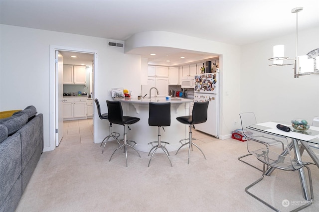 kitchen with white cabinetry, light colored carpet, decorative light fixtures, white appliances, and a kitchen bar