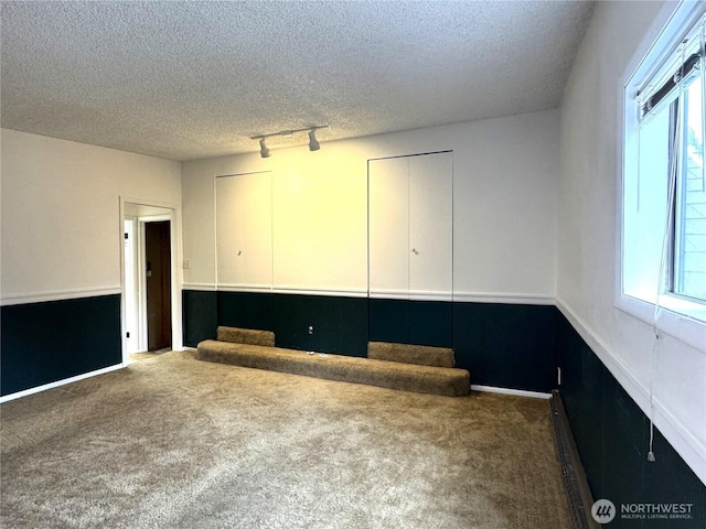 carpeted spare room with track lighting, baseboards, baseboard heating, and a textured ceiling