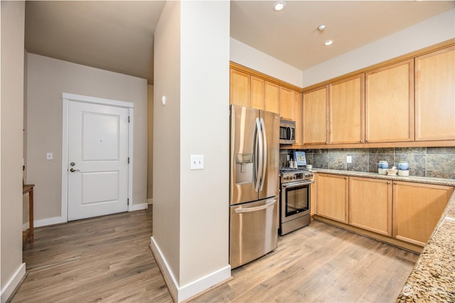 kitchen featuring light brown cabinets, backsplash, light stone countertops, light wood-type flooring, and appliances with stainless steel finishes