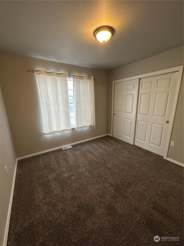 unfurnished bedroom with a closet, a textured ceiling, and dark colored carpet