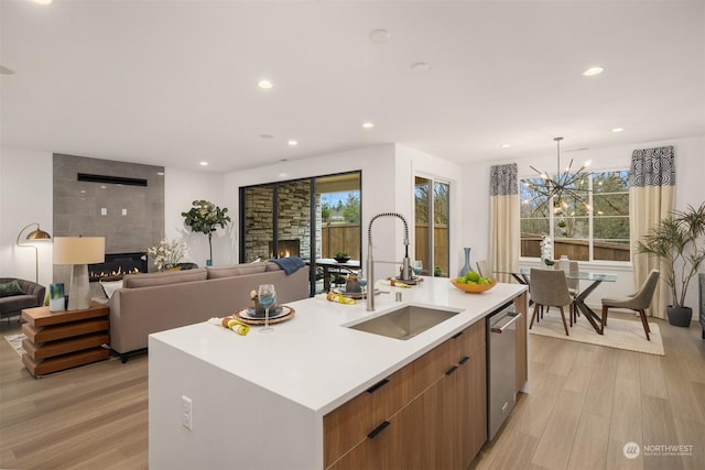 kitchen with light wood-type flooring, sink, a tile fireplace, dishwasher, and an island with sink