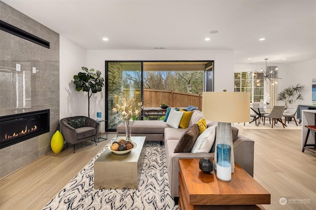 living room featuring light hardwood / wood-style flooring, a notable chandelier, and a tiled fireplace