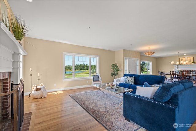 living room featuring light hardwood / wood-style floors, a notable chandelier, and a brick fireplace