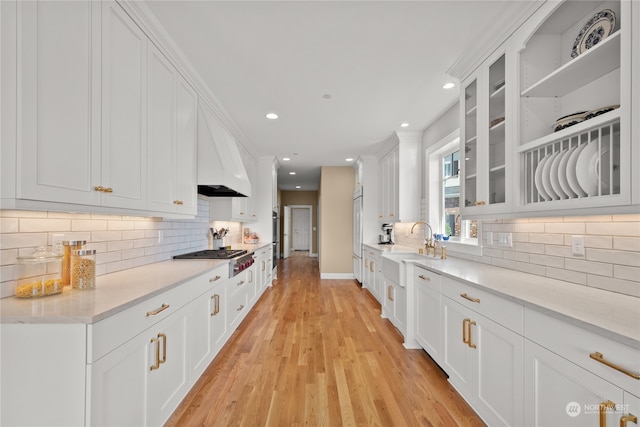 kitchen with stainless steel gas stovetop, white cabinets, tasteful backsplash, light hardwood / wood-style floors, and light stone counters