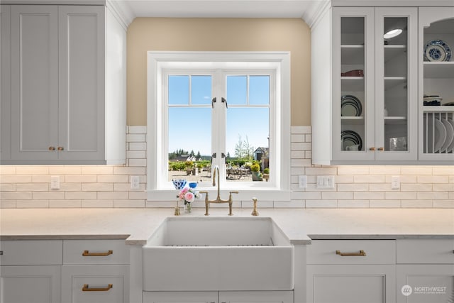 kitchen with tasteful backsplash, white cabinetry, sink, and light stone countertops