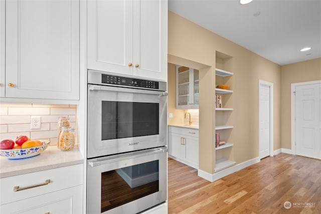 kitchen featuring double oven, backsplash, white cabinets, and light wood-type flooring