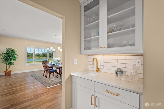 bar featuring sink, hanging light fixtures, light hardwood / wood-style floors, decorative backsplash, and white cabinets