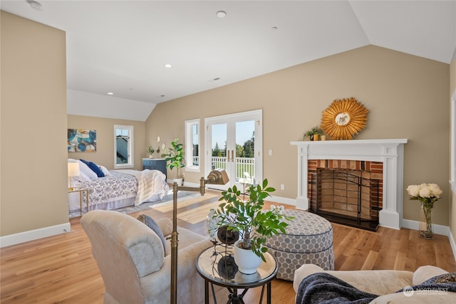 living room with french doors, light hardwood / wood-style floors, lofted ceiling, and a brick fireplace