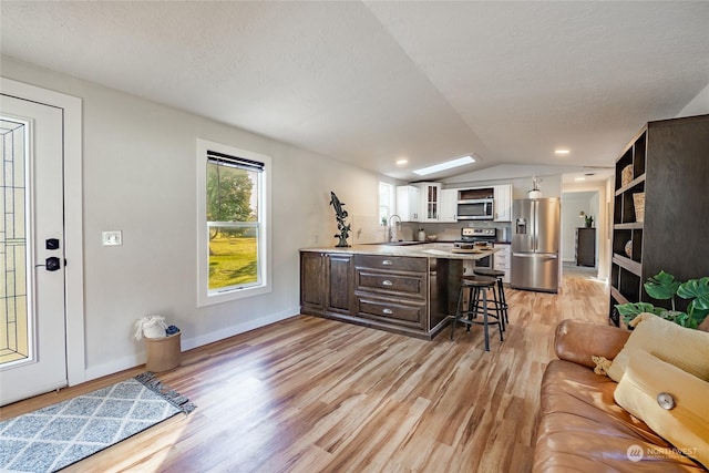 kitchen with a kitchen bar, lofted ceiling, stainless steel appliances, and dark brown cabinetry