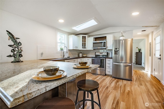 kitchen featuring tasteful backsplash, stainless steel appliances, lofted ceiling with skylight, sink, and white cabinetry