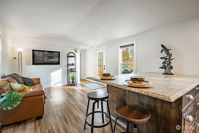 living room with a textured ceiling, light hardwood / wood-style flooring, vaulted ceiling, and wood walls