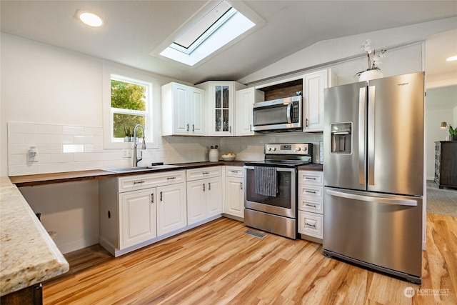 kitchen featuring vaulted ceiling with skylight, white cabinetry, sink, and appliances with stainless steel finishes