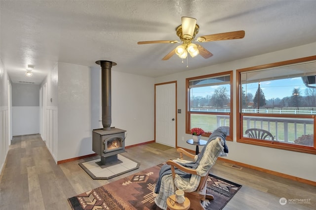 living room with a wood stove, ceiling fan, a textured ceiling, and light wood-type flooring