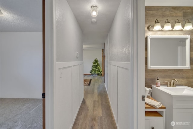 hall with sink, light wood-type flooring, and a textured ceiling