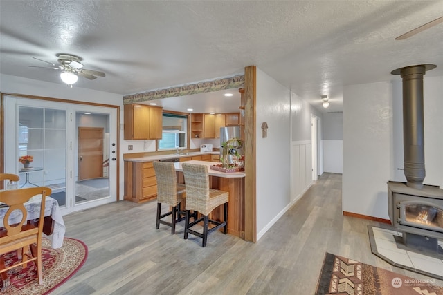 kitchen with a breakfast bar, a wood stove, light wood-type flooring, a textured ceiling, and stainless steel refrigerator