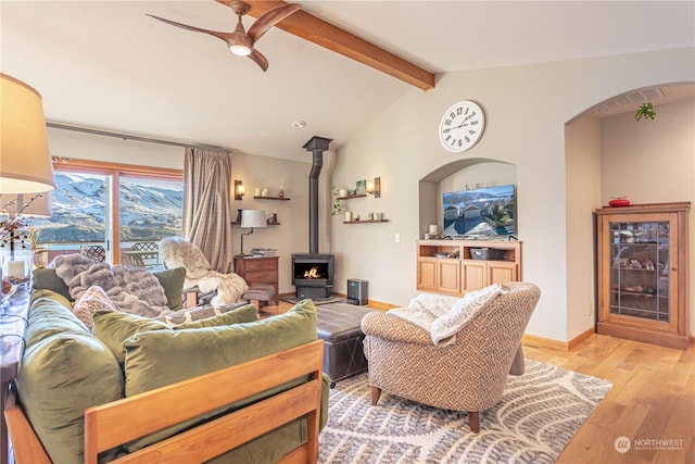 living room with light wood-type flooring, lofted ceiling with beams, a wood stove, and ceiling fan