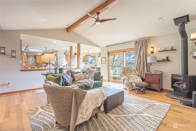 living room featuring light wood-type flooring, lofted ceiling with beams, a wood stove, and ceiling fan