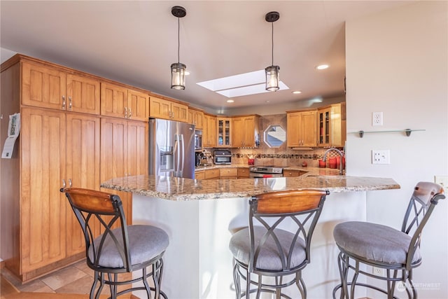 kitchen featuring kitchen peninsula, appliances with stainless steel finishes, decorative backsplash, light stone counters, and sink