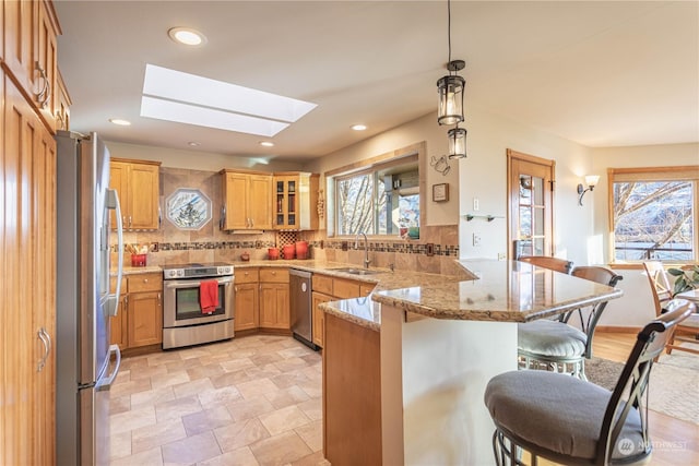 kitchen featuring kitchen peninsula, appliances with stainless steel finishes, a skylight, sink, and hanging light fixtures