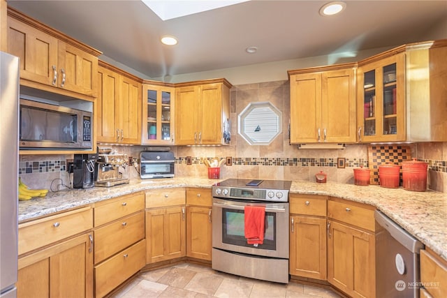 kitchen featuring backsplash, a skylight, light stone countertops, and appliances with stainless steel finishes