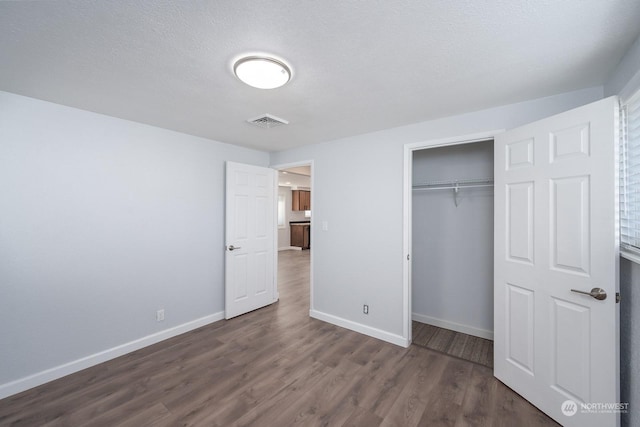 unfurnished bedroom with a textured ceiling, a closet, and dark wood-type flooring