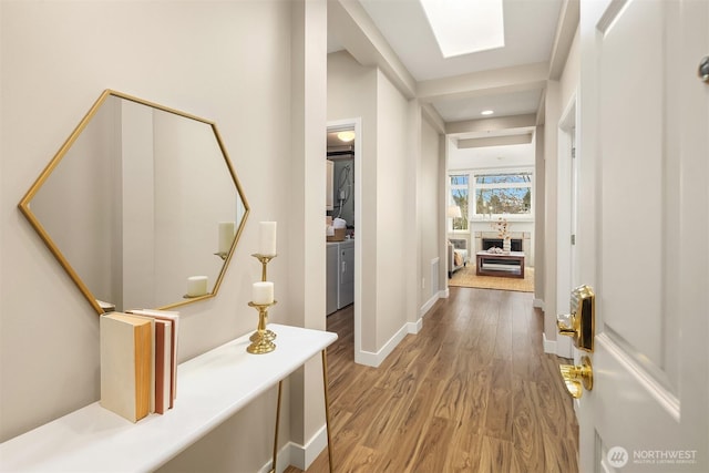 hall featuring stacked washer and clothes dryer, a skylight, baseboards, and wood finished floors