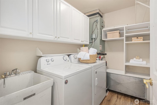 laundry area with washing machine and clothes dryer, light wood-style flooring, cabinet space, and a sink