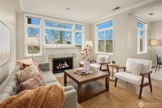 interior space with visible vents, light wood-style flooring, a tiled fireplace, crown molding, and baseboards