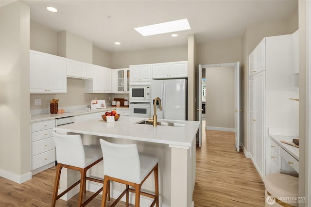 kitchen with light wood finished floors, white appliances, a skylight, and a sink