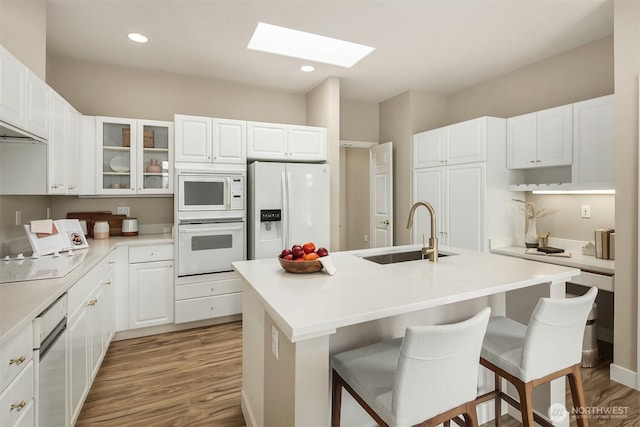 kitchen with white appliances, a skylight, a kitchen breakfast bar, and a sink