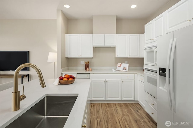 kitchen featuring light wood finished floors, recessed lighting, white refrigerator with ice dispenser, white cabinets, and a sink