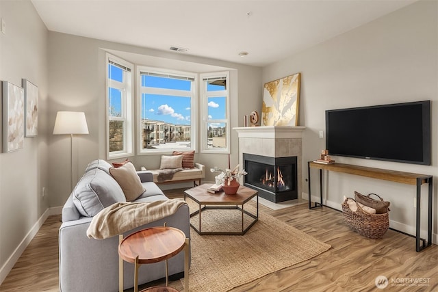 living area with visible vents, a tile fireplace, baseboards, and wood finished floors