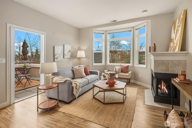 living room with baseboards, wood finished floors, visible vents, and a tile fireplace