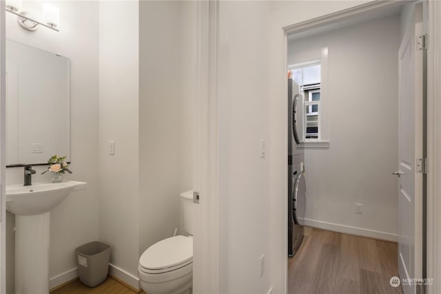 bathroom featuring wood-type flooring, stacked washing maching and dryer, and toilet