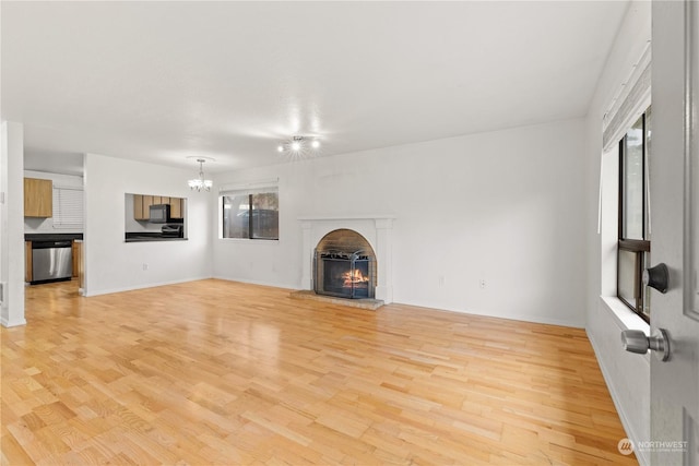 unfurnished living room with a chandelier, light wood-type flooring, and a brick fireplace