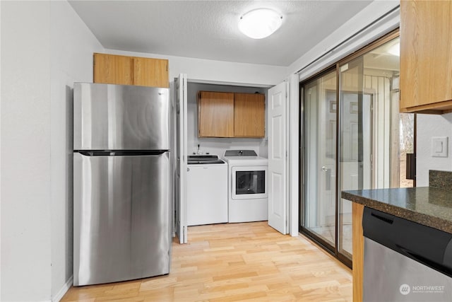 kitchen with appliances with stainless steel finishes, a textured ceiling, light hardwood / wood-style flooring, and washer and clothes dryer