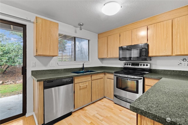 kitchen with appliances with stainless steel finishes, a textured ceiling, sink, light brown cabinets, and light hardwood / wood-style floors