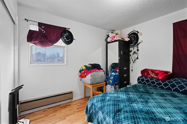 bedroom featuring hardwood / wood-style floors, a textured ceiling, and a baseboard heating unit