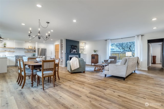 dining area with a large fireplace, light hardwood / wood-style floors, and a notable chandelier