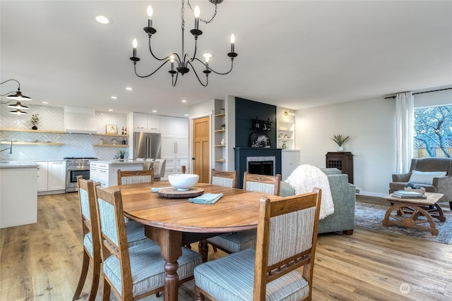 dining area with a fireplace, light wood-type flooring, and a notable chandelier